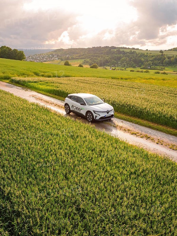 A car drives on a dirt track through a rape field under a cloudy sky, Deer E- CarSharing, Renault Megane electric car, Calw, Black Forest, Germany