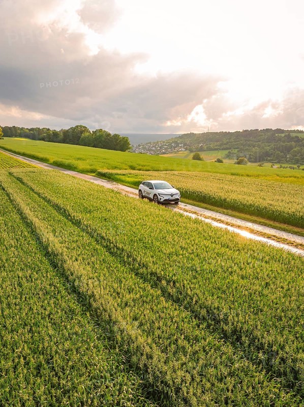 A car drives on a narrow road along green fields under a cloudy sky, Deer E- CarSharing, Renault Megane electric car, Calw, Black Forest, Germany