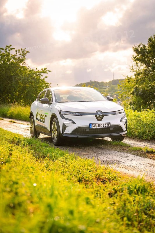 White car on a rural road with green meadows and cloudy sky in the background, Deer E- CarSharing, Renault Megane electric car, Calw, Black Forest, Germany