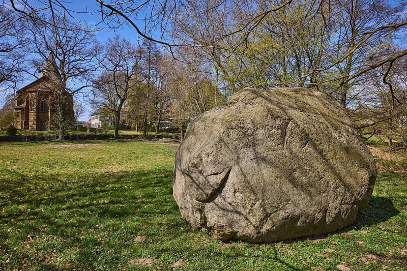 Boulder from southern Sweden, granite, Saale Ice Age, lawn, bare winter trees, blue cloudless sky, Pfarrer-Dustmann-Straße, Bad Oeynhausen, Mühlenkreis Minden-Lübbecke, North Rhine-Westphalia, Germany