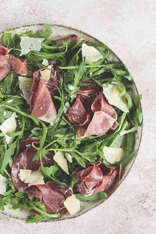 Fresh arugula salad with prosciutto and grated parmesan cheese, on a plate, homemade, no people