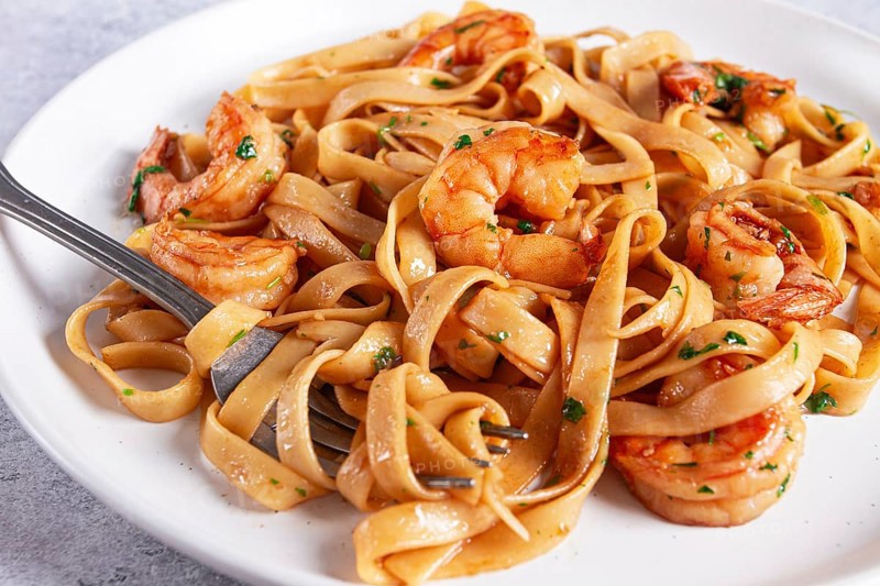 Fettuccine pasta with shrimp, spicy in soy sauce, on a grey plate with a fork, close-up