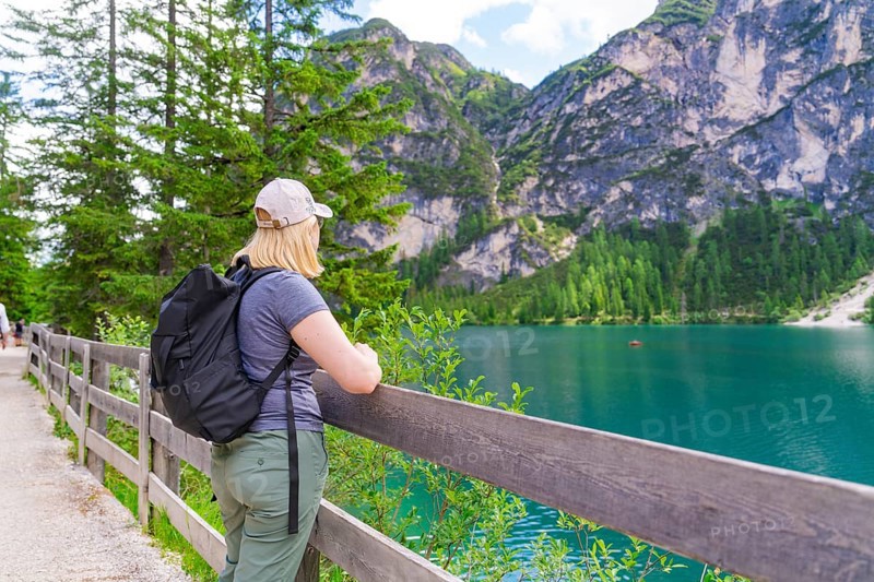 Person looking from a wooden fence at a mountain lake, surrounded by nature, Lake Braies, South Tyrol, Dolomites, Italy