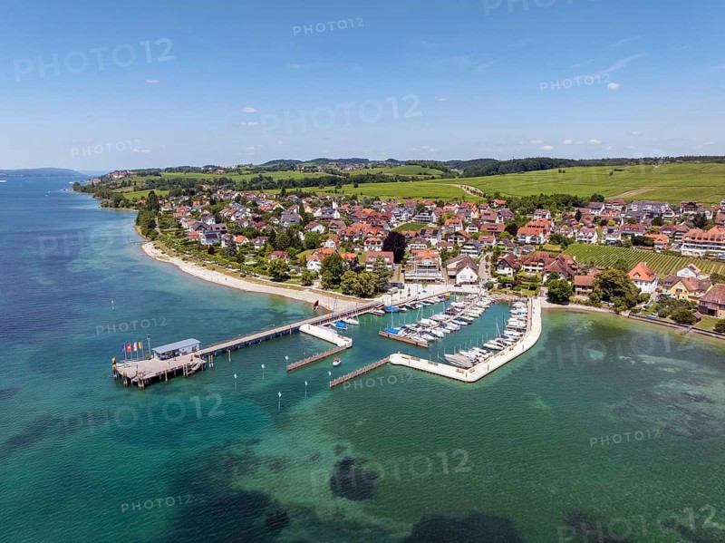 Luftbild von der Bodenseegemeinde Hagnau, Winzerdorf und beliebter Ferienort am Bodensee, dahinter Rebhänge, auf denen hauptsächlich die Weinsorten Müller Thurgau und Blauer Burgunder angebaut werden. Am Seeufer der am 23.Mai 2025 eingeweihte, neue Westhafen, Yachthafen mit der Schiffanlegestelle, Bodenseekreis, Baden-Württemberg, Deutschland