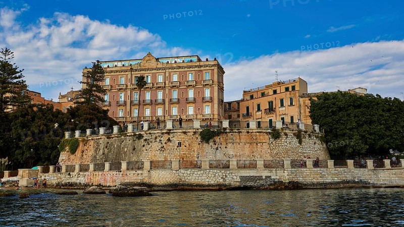 Elevated wall with historic buildings and lush vegetation in the coastal area, boat trip around the island of Ortigia, Isola di Ortigia, Syracuse, Sicily, Italy