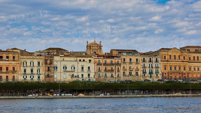 Rows of historic buildings along a coastal promenade under a patterned sky, boat trip around the island of Ortigia, Isola di Ortigia, Syracuse, Sicily, Italy