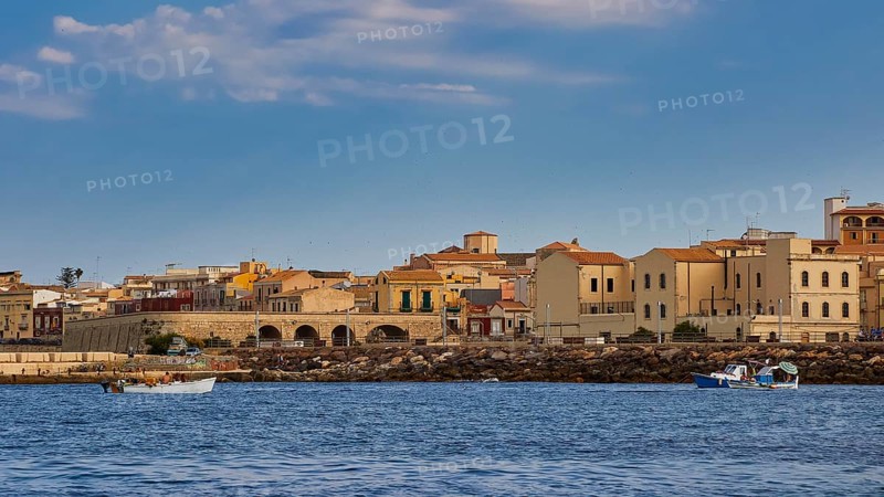 Town by the sea with old buildings and small boats, blue sky above, boat trip around the island of Ortigia, Isola di Ortigia, Syracuse, Sicily, Italy