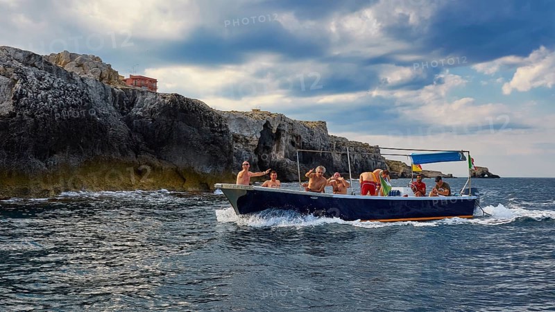 Group of people on a boat near rocky cliffs, boat trip around the island of Ortigia, Isola di Ortigia, Syracuse, Sicily, Italy