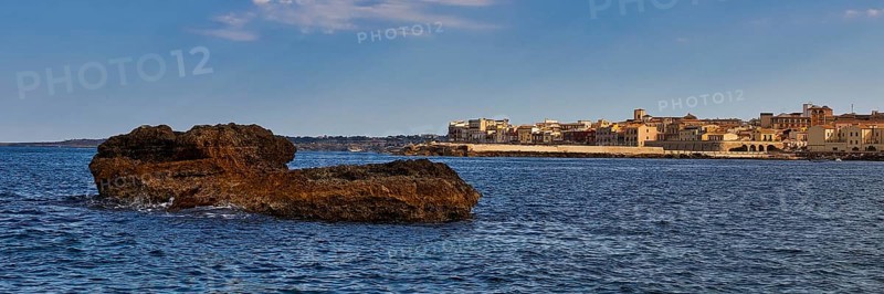 Coastal cliffs in the foreground with a town and blue sky in the background, boat trip around the island of Ortigia, Isola di Ortigia, Syracuse, Sicily, Italy