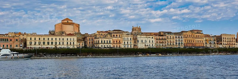 Coastal view with historic buildings against a cloudy blue sky on the promenade, boat trip around the island of Ortigia, Isola di Ortigia, Syracuse, Sicily, Italy