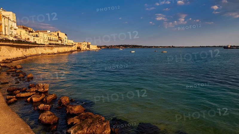 Coastline with rocks and buildings in the warm evening light under a clear sky, Ortigia Island, Isola di Ortigia, Historic old town, Syracuse, Sicily, Italy