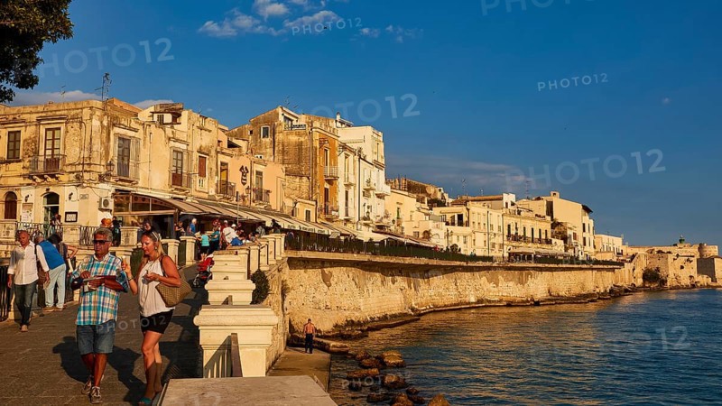 People walking along the coastal promenade with historic buildings in the evening light, Ortigia Island, Isola di Ortigia, Historic old town, Syracuse, Sicily, Italy
