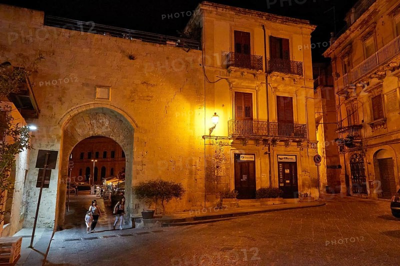 Night scene of an illuminated historic alley and a large gate with cobblestones and lantern light, Ortigia Island, Isola di Ortigia, Historic Old Town, Syracuse, Sicily, Italy