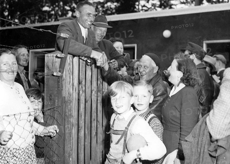 Refugees from the Soviet zone, 1952, A group of people gather around a fence, some smile and shake hands, historical photo