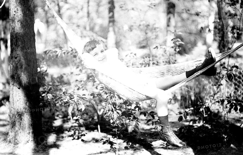 Boy lying in hammock, 1920s, Smiling child lying in a hammock in the forest, Historical photo
