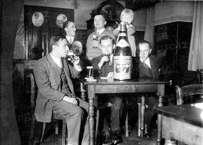 Male company and girls, 1920s, group of men celebrating together with large bottle and glasses in hand, historical photo