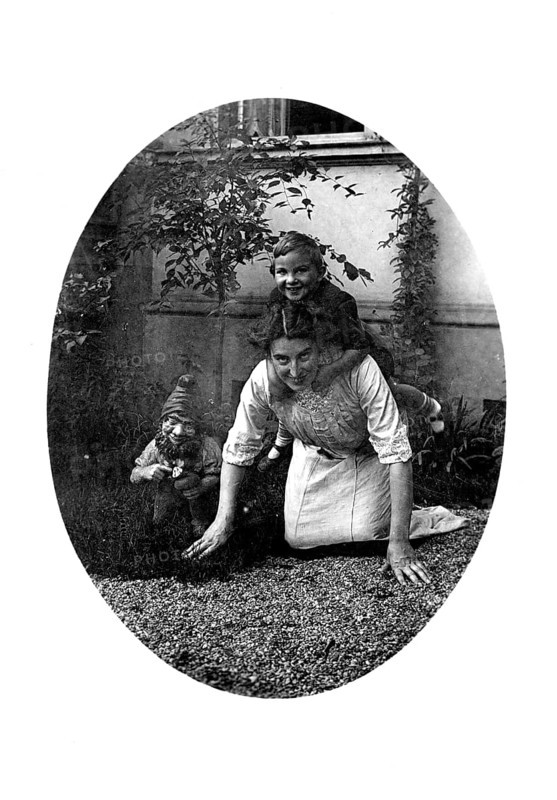 Woman carrying a child on her back, 1920s, A woman crawls on the floor with a child on her back, accompanied by a dwarf figure, Historical photo