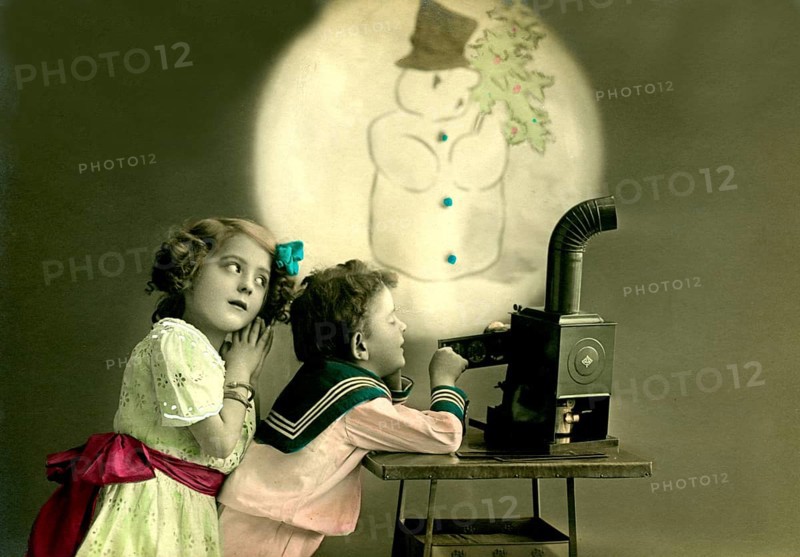 Children's slide projector snowman, 1912, Two children watching a snowman projection, nostalgic atmosphere with an old projector, historical photo