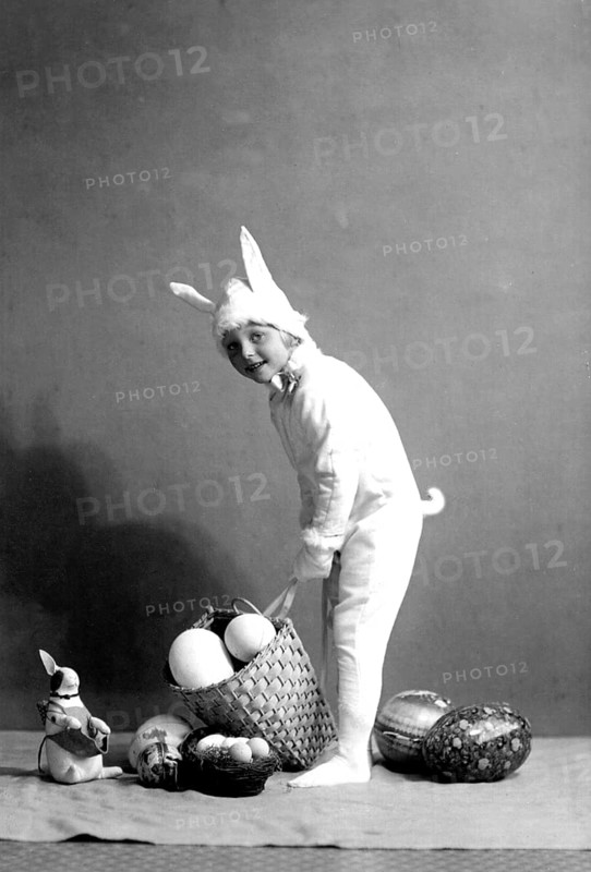 Girl dressed up as an Easter bunny, 1930s, A child in a bunny costume places a basket of eggs on the floor, Historical photo