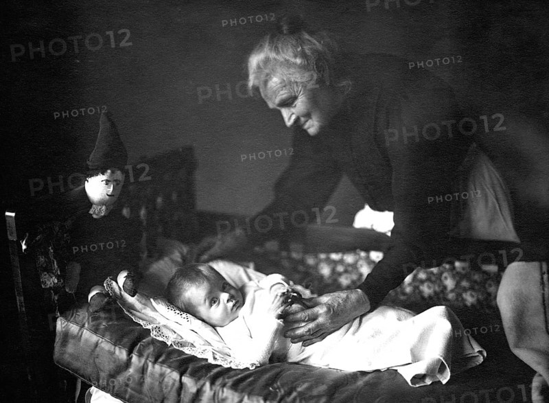 Grandma with grandson, 1930s, An elderly woman lovingly cares for a baby in a cradle, Historical photo