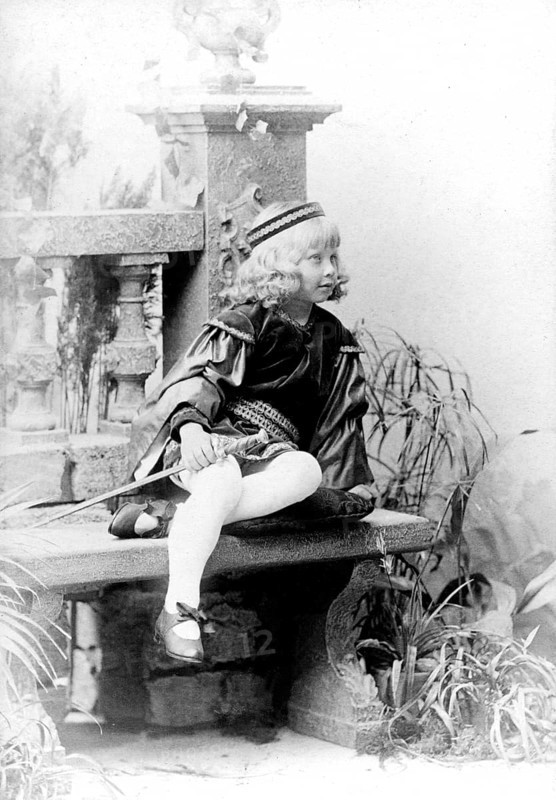 Dressed up girl with sword, 1930s, child in costume sitting on a stone bench, black and white scene with decorative elements, historical photo