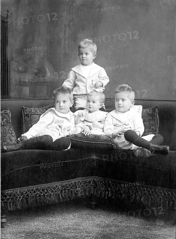 Small children sitting on sofa, 1930s, Four children in classic clothes sitting together on a couch and looking seriously into the camera, Historical photo