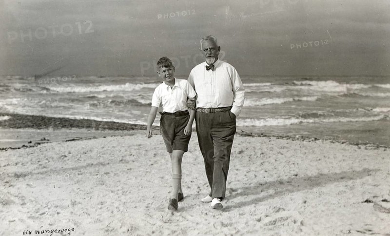Grandpa and grandson on the beach of Wangerooge, 1930s, Elderly man and boy walking along the beach, the sea in the background, Historical photo