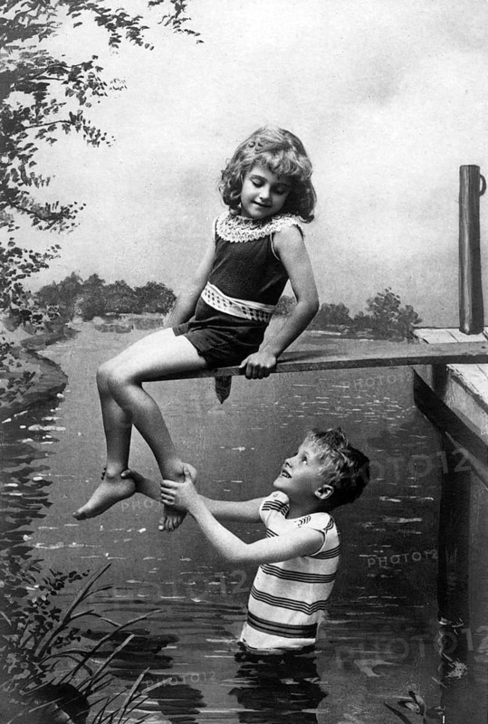 Boy holding girl by the foot, 1920, A boy happily lifting a girl, both in swimwear enjoying the summer on the river bank, Historical photo