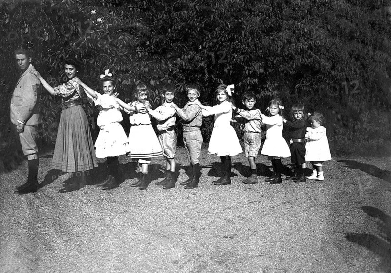 Large family posing in size, organ pipes, 1920s, children in a row, holding each other by the shoulders. Historical clothing and cheerful atmosphere outdoors, historical photo