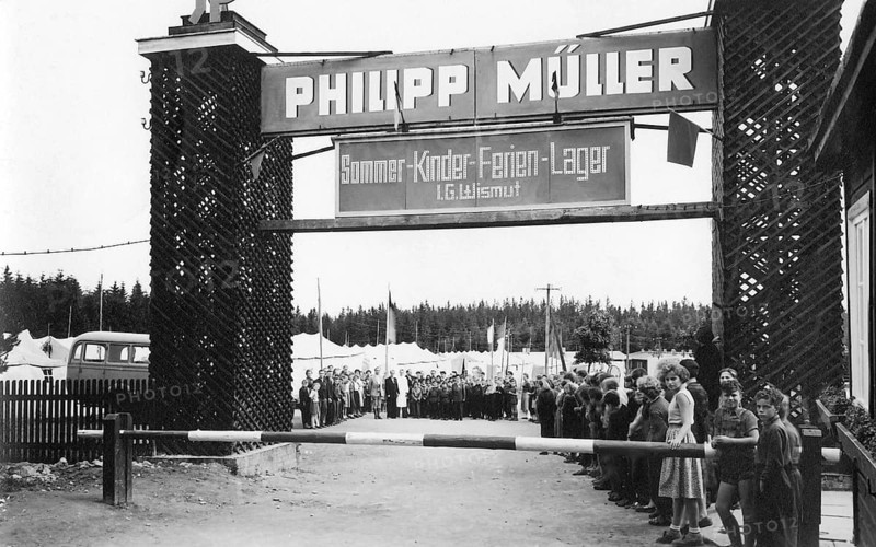 Summer children's holiday camp, 1930s, people standing in two rows in front of an entrance with a banner, tents and trees can be seen in the background, historical photo