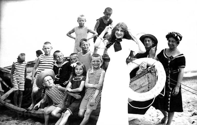 Children's leisure time, 1920s, children in striped clothes and a woman posing smiling on the beach next to an old boat, historical photo