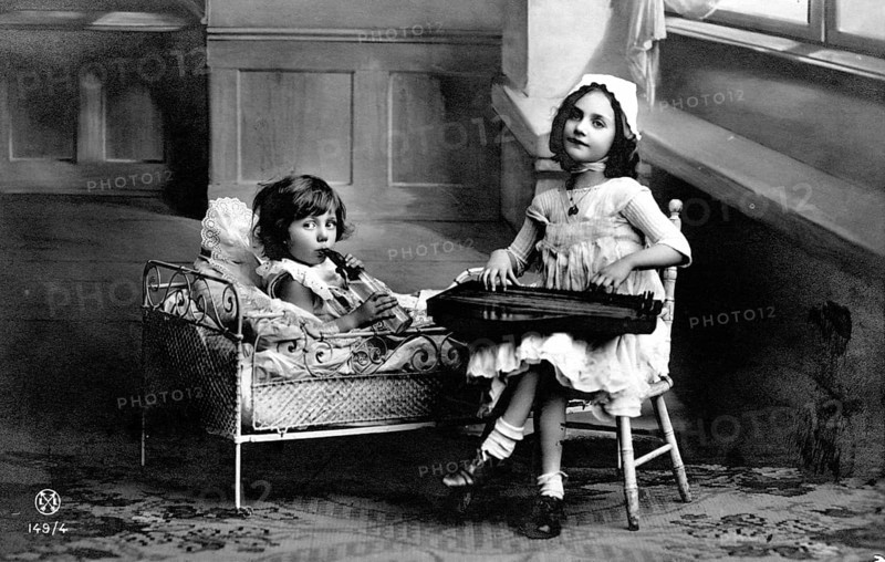 Two children making music, 1920s, Two girls, one in bed and one on a chair, playing in an old interior, Historical photo