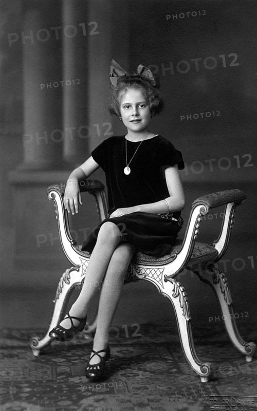Distinguished girl, 1920, A girl sits solemnly on an ornately decorated chair, wearing a pearl necklace, Historical photo