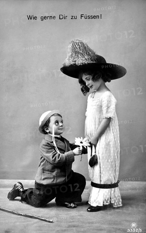 Boy kneeling in front of girl, 1910, A boy with flowers kneeling in front of a girl in a big hat, Historical photo