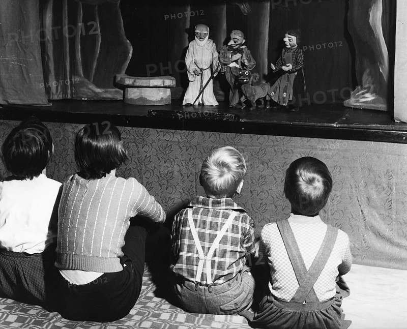 Children watching puppet theatre, 1960s, Children sitting in front of a puppet stage and watching a performance, historical photo
