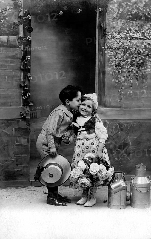Boy kisses girl, 1920s, A boy kisses a girl on the cheek, surrounded by flowers and pewter cans, Historical photo
