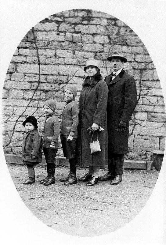 Family standing in a row, 1930s, Family in winter clothes standing together in front of a stone wall in black and white, Historical photo