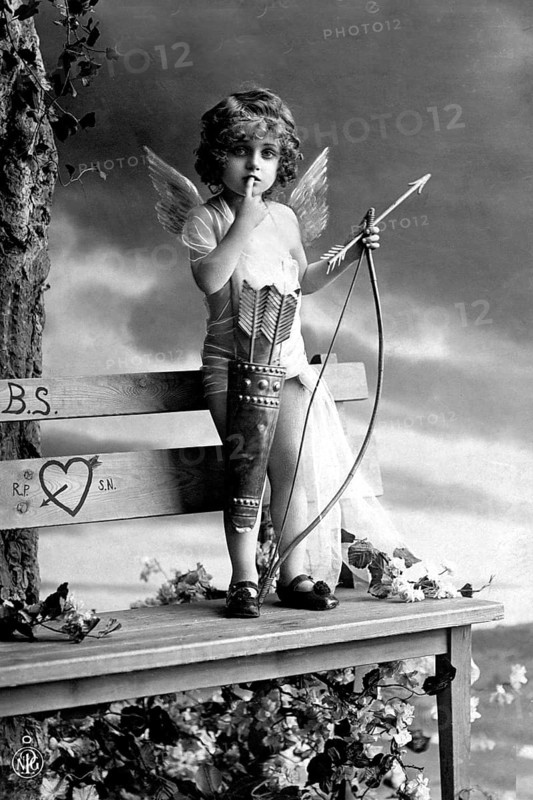Little boy as Cupid, 1920s, A child dressed as Cupid, with wings and bow, standing on a bench, Historical photo