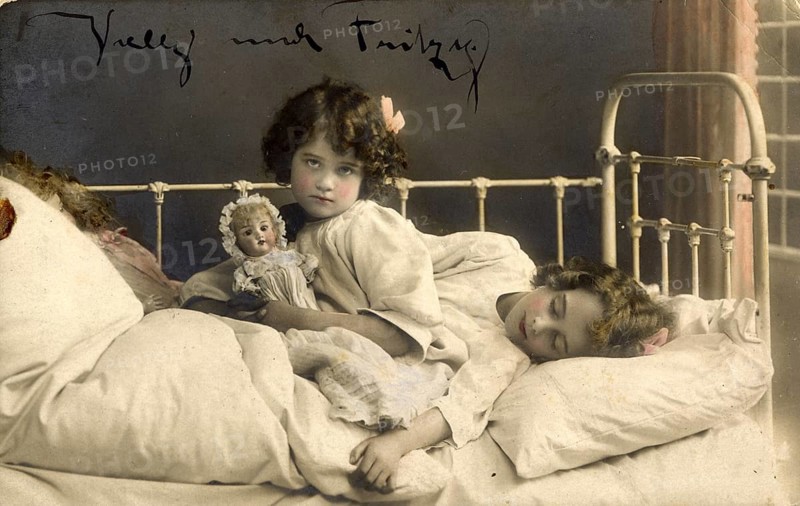 Two girls in bed, 1920s, Two children in bed, one awake with doll, the other asleep, atmospheric, Historical photo