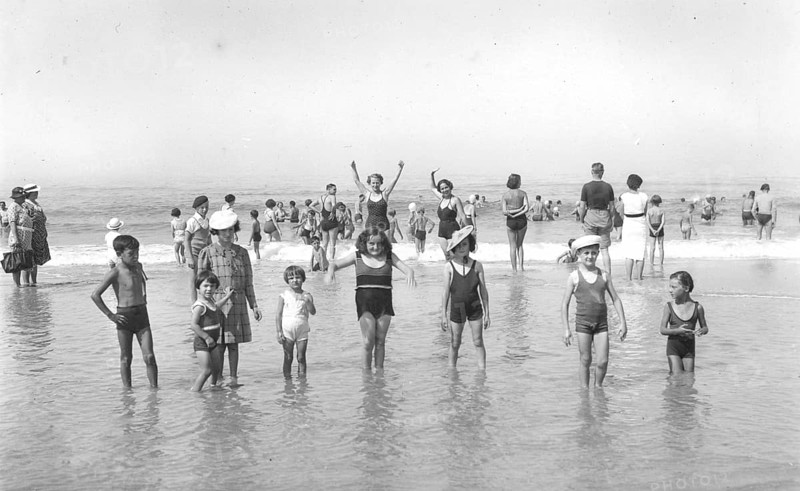 Children in the water, 1920s, Children playing in shallow water on the beach under a clear sky. A cheerful summer scene, historical photo