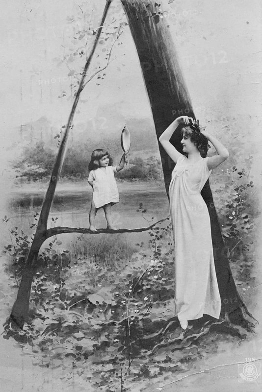 Looking in the mirror, 1920s, A woman and a child holding a hand mirror pose in front of a tree in a dreamy scene, Historical photograph
