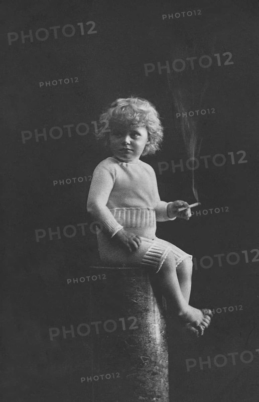 Child smoking, 1920s, A child in historical clothing sits on a pedestal and holds a cigarette in his hand, Historical photo