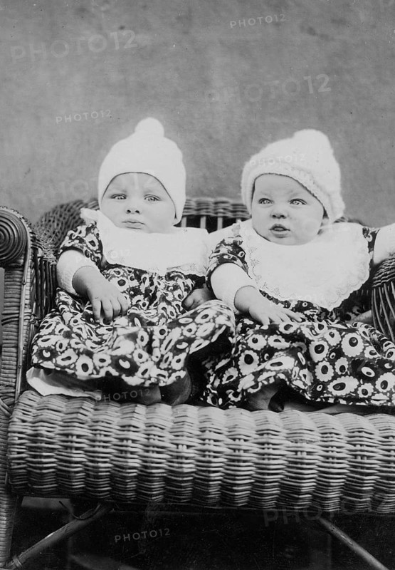 Two wrapped-up babies, 1930s, Two babies in old-fashioned clothes and caps on a wicker chair, Historical photo