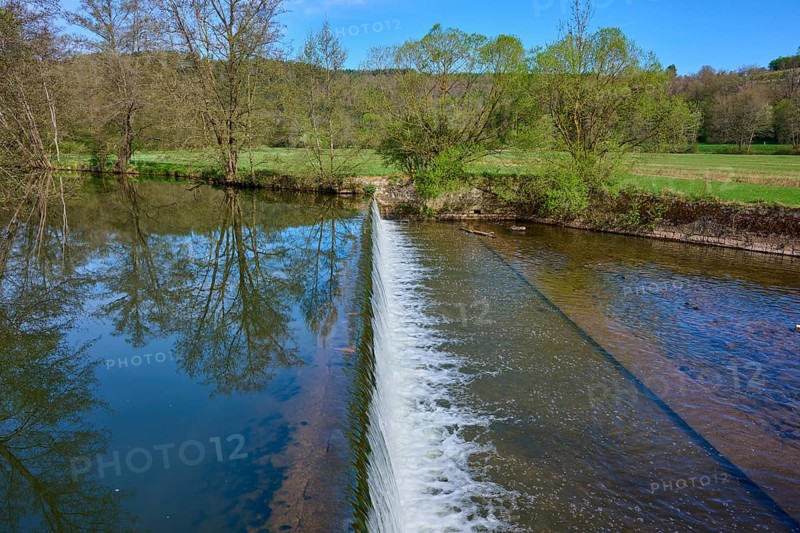 Small dam wall with falling water and reflection of the trees in the river, spring, Obersinn, Sinntal, Spessart, Bavaria, Germany