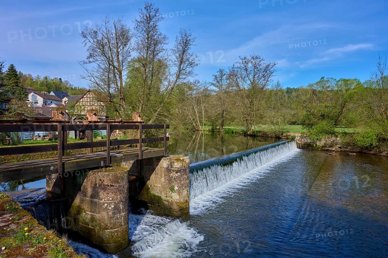 A weir bridges a river, surrounded by fresh green trees, spring, Obersinn, Sinntal, Spessart, Bavaria, Germany