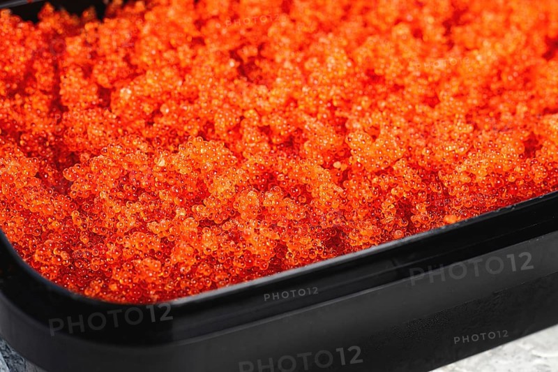 Container with orange caviar, flying fish, Tobiko, on the table, caviar for rolls and sushi, close-up