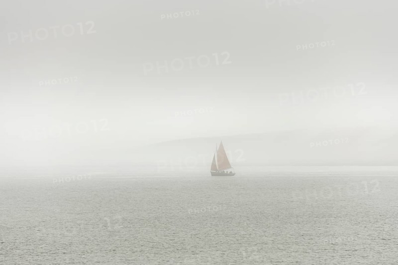 A sailing boat is travelling on the ocean on a cloudy day. The sky is overhanging and the water is calm. Camaret sur mer, Crozon, Finistere, Brittany, France