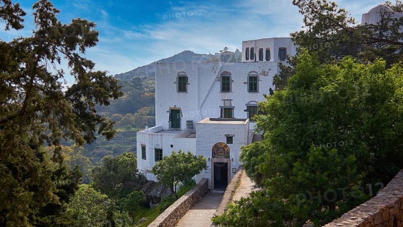 White monastery building surrounded by dense vegetation and a sunny sky, Monastery of the Revelation, Moni tis Apokalipsis, World Heritage Site 1999, Patmos, Dodecanese, Greek Islands, Greece