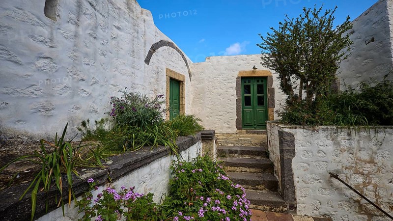 Inner courtyard with whitewashed walls, green doors and flowering plants, Monastery of the Revelation, Moni tis Apokalipsis, World Heritage Site 1999, Patmos, Dodecanese, Greek Islands, Greece