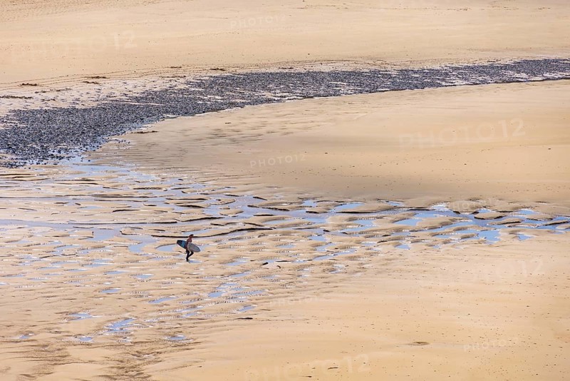 Man with a surfboard walking on a sand beach on the way to the sea a sunny summer day, Crozon peninsula, Bretagne, France